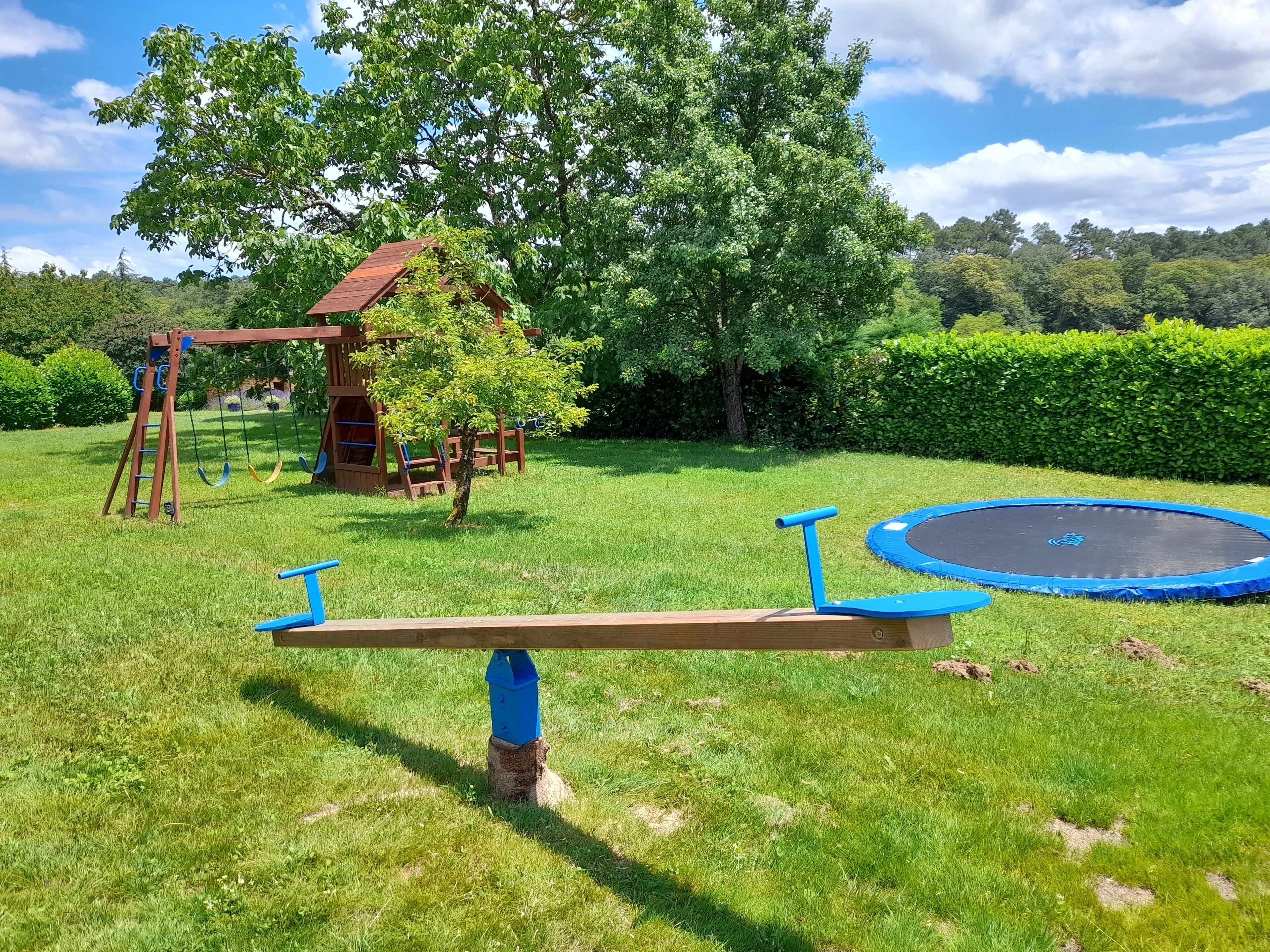 A playground with a seesaw, trampoline, and wooden playhouse.