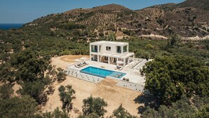 A modern villa with a pool, surrounded by hills and trees.