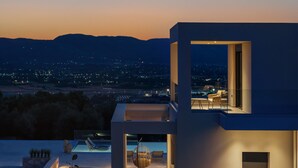 A modern building with a pool, outdoor seating, and a view of the city at dusk.