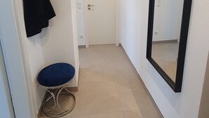 A hallway with a white door, a black coat hanging on the wall, a blue stool, and a large mirror. - Bright, newly renovated TOP flat in a central location (Osnabrück)