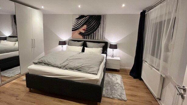 A modern bedroom with a large bed, bedside tables, a wardrobe, and a large mirror. - Bright, newly renovated TOP flat in a central location (Osnabrück)