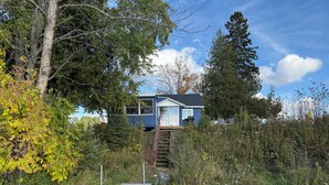 A house with a wooden deck and a staircase leading to a second-story window. - Swimming, Snowmobiling, Serenity! Lakefront Cottage on Big Manistique Lake (McMillan)