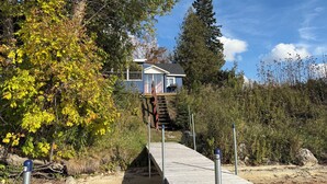 A house with a wooden deck leading to a raised platform, surrounded by trees and vegetation. - Swimming, Snowmobiling, Serenity! Lakefront Cottage on Big Manistique Lake (McMillan)