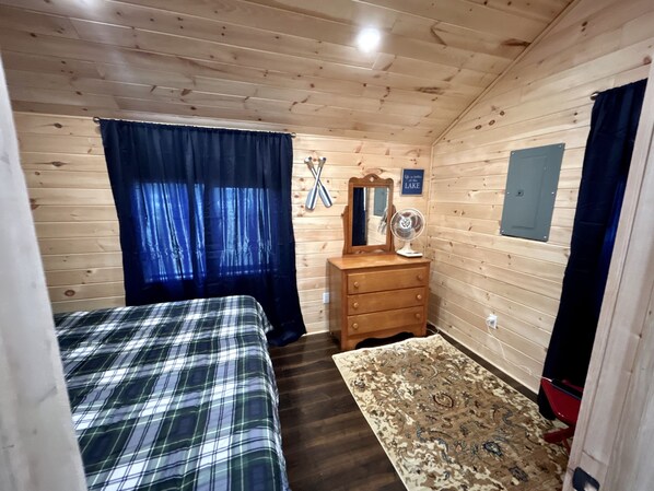 A wooden cabin bedroom with two beds, a dresser, a mirror, and a fan. - Swimming, Snowmobiling, Serenity! Lakefront Cottage on Big Manistique Lake (McMillan)