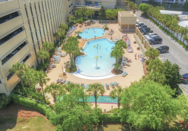 A rooftop pool area with multiple pools, lounge chairs, and palm trees.