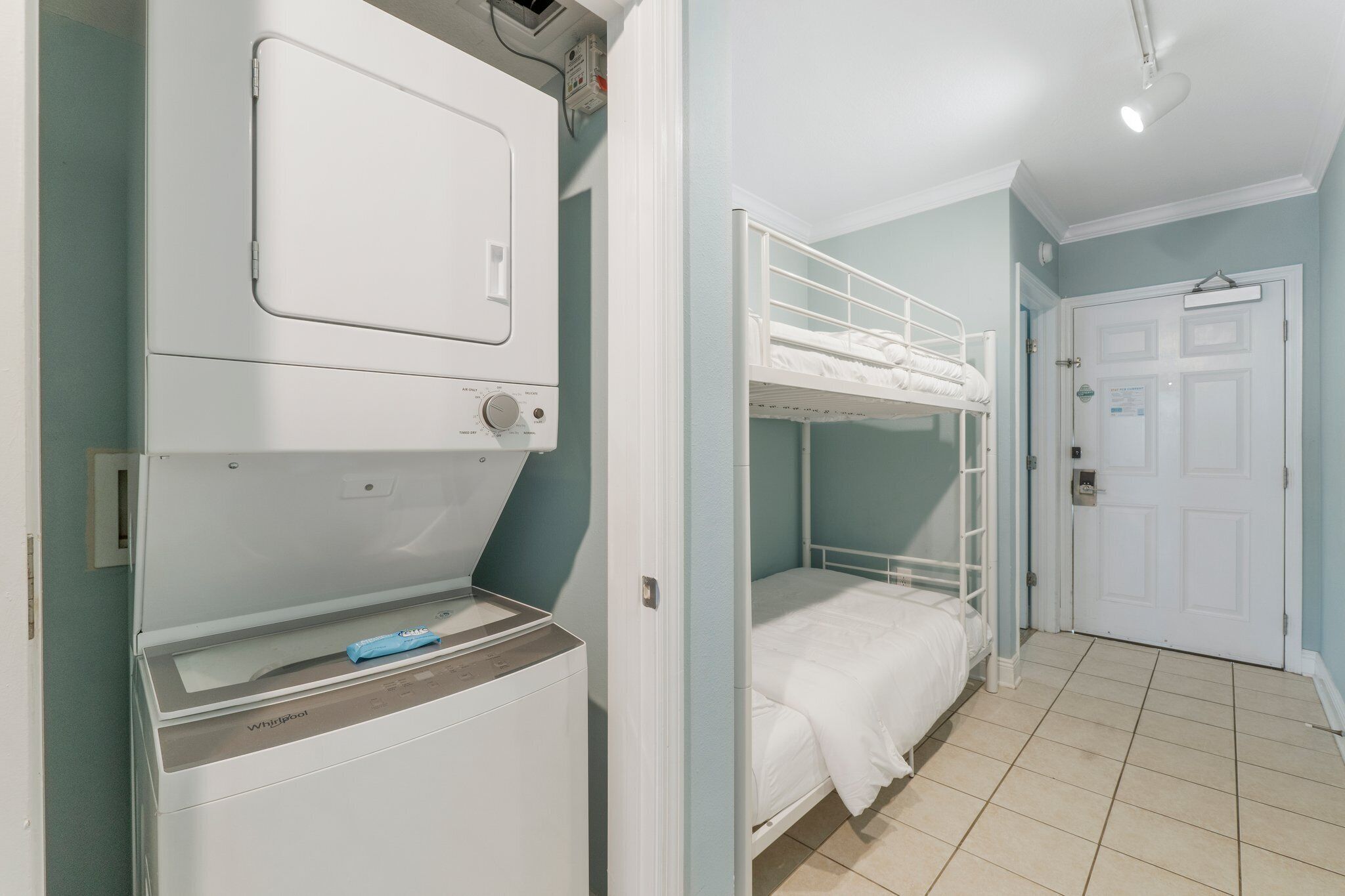 Une pièce avec un lit superposé, un lave-linge et une porte.