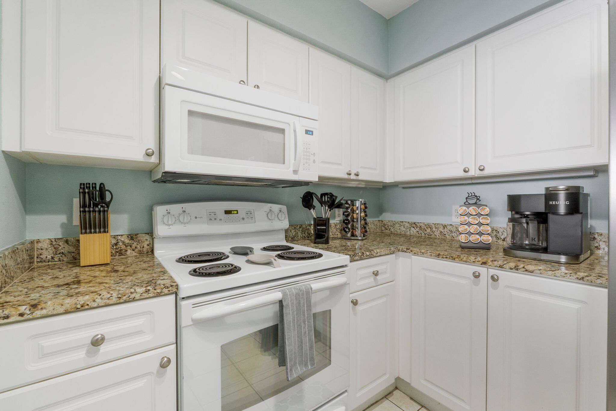 A kitchen with white cabinets, a white stove, a microwave, and a coffee maker.