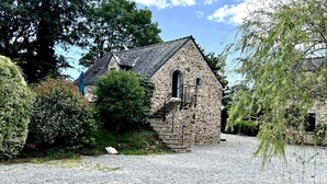 Un bâtiment en pierre doté d’un toit en pente, entouré de gravier et de verdure.