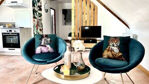 Un salon moderne avec deux fauteuils turquoise, une petite table blanche et un téléviseur.