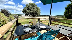 Un espace de restauration en plein air avec une table dressée pour deux personnes, des chaises et un grand parasol.