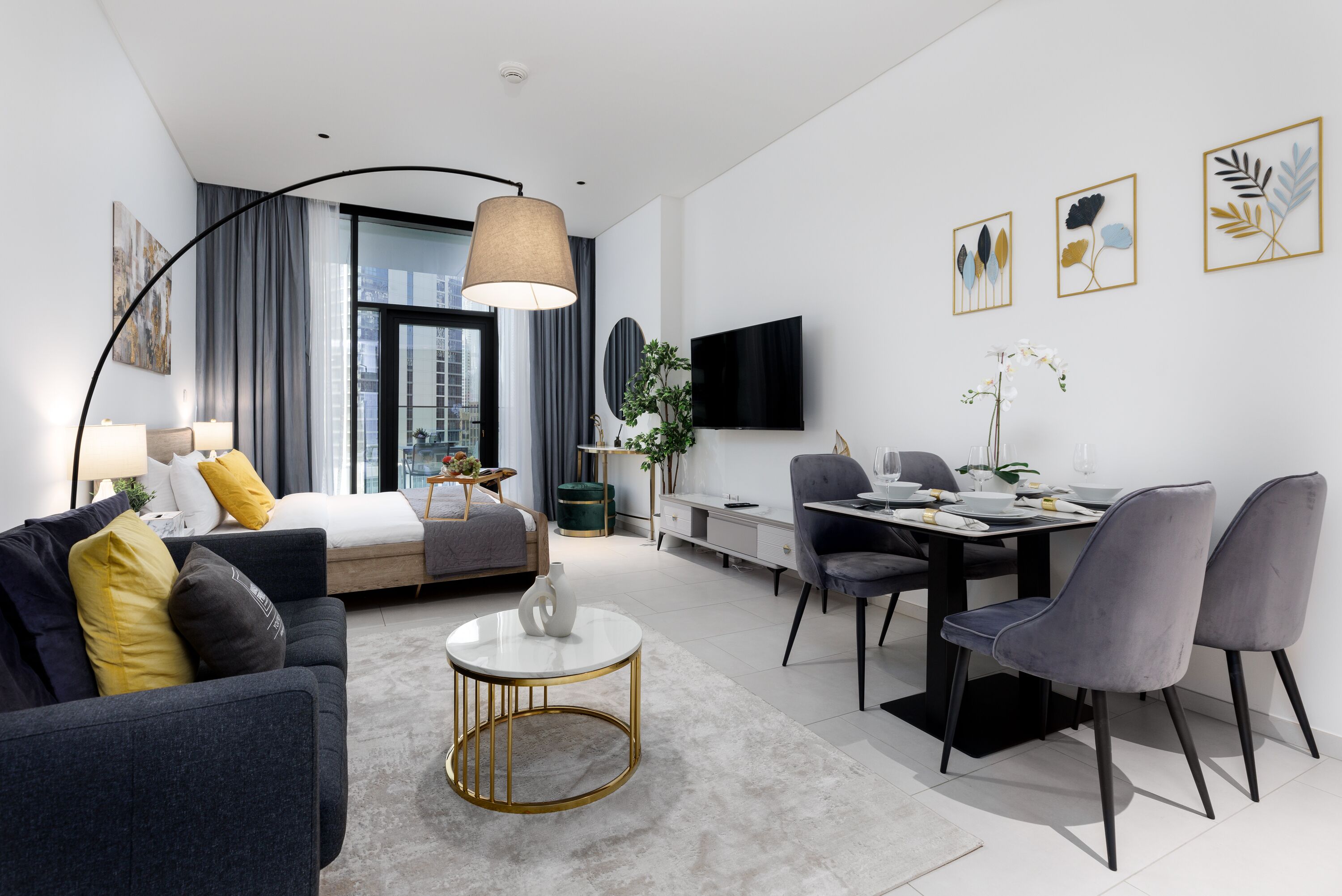 Una habitación de hotel moderna con cama, sofá, zona de comedor y televisión en la pared.