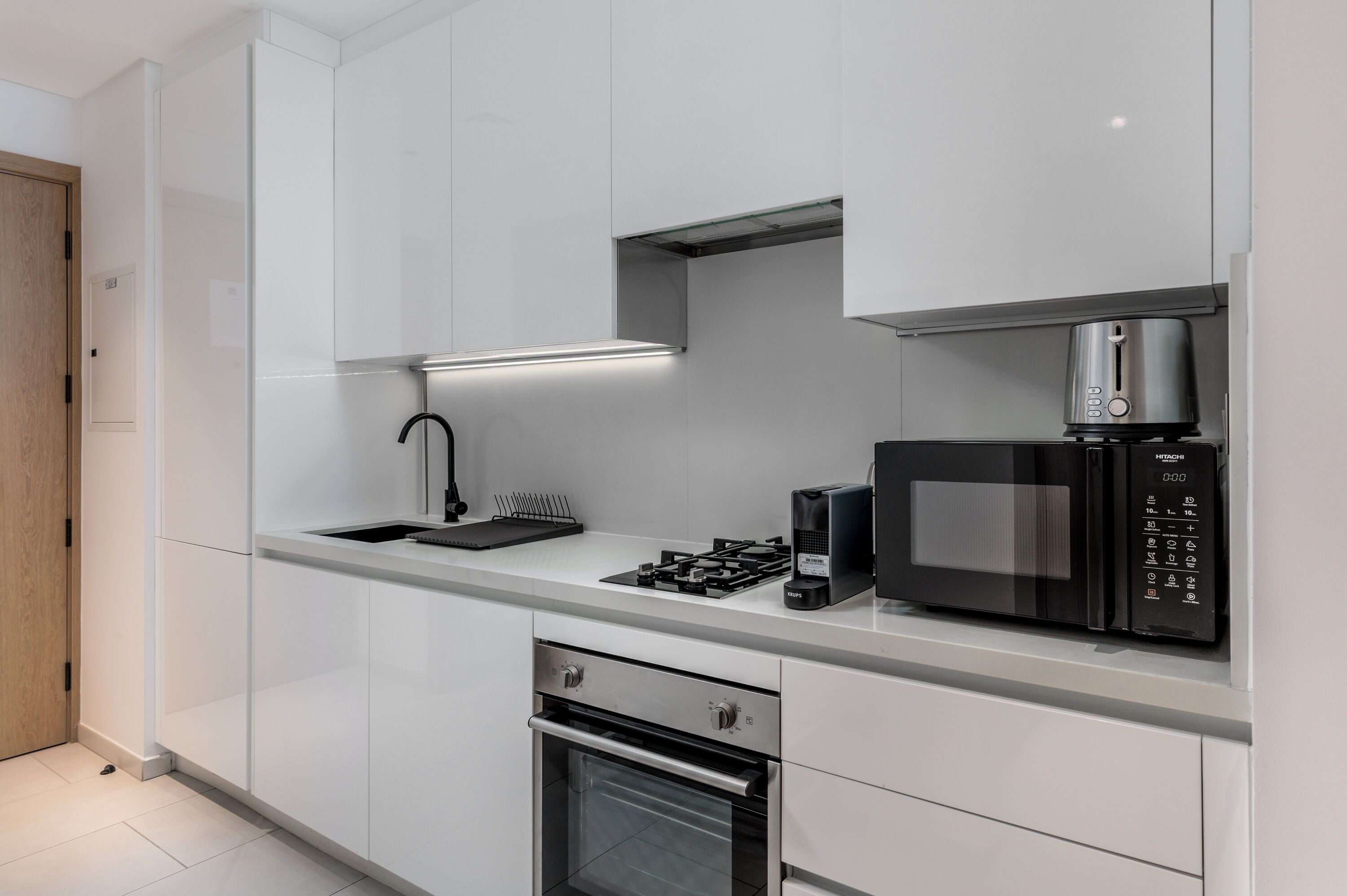 Una cocina moderna con armarios blancos, un microondas integrado, una estufa a gas y un horno de acero inoxidable.