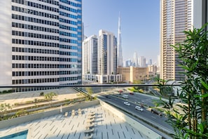 A modern urban area with high-rise buildings, a wide road, and a landscaped area with seating. - Maison Privee - Premium Studio w/ Burj Khalifa View (Dubai)