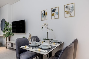 A modern dining area with a rectangular table set for four, surrounded by grey upholstered chairs. A flat-screen TV is mounted on the wall above the table. - Maison Privee - Premium Studio w/ Burj Khalifa View (Dubai)