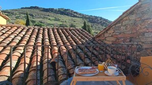 A terrace with a tiled roof, a table with breakfast items, and a stone wall. - El Mirador de las Jaras (Patones)