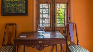 A wooden table with a glass and a book, flanked by two chairs with patterned cushions, against an orange wall with a framed painting. - El Mirador de las Jaras (Patones)