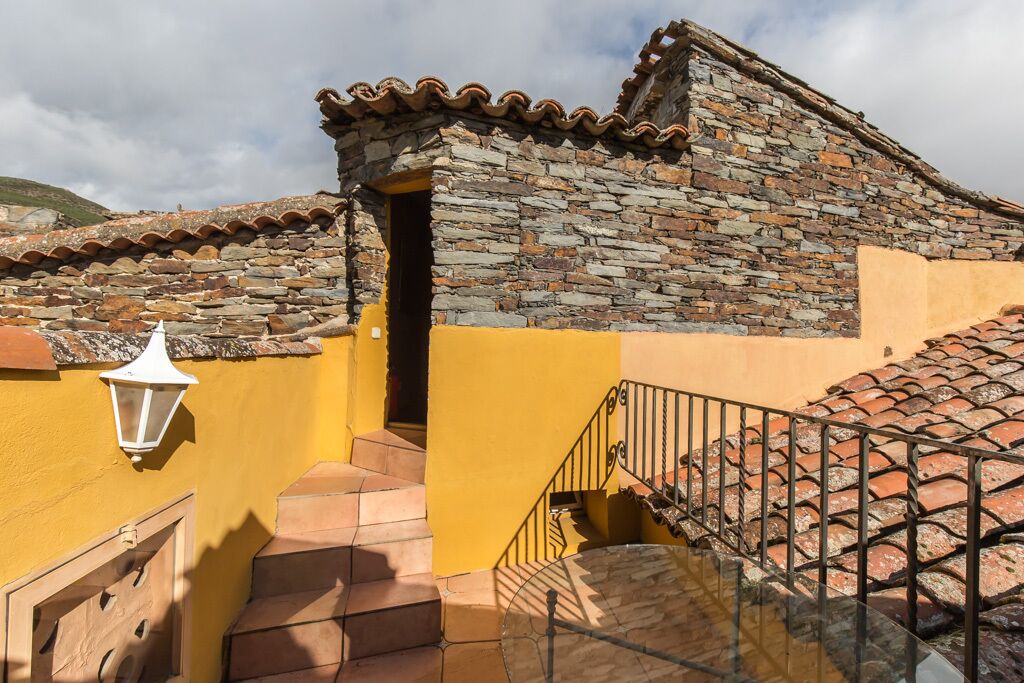 A stone building with a yellow exterior, a tiled roof, and a staircase leading to an entrance.