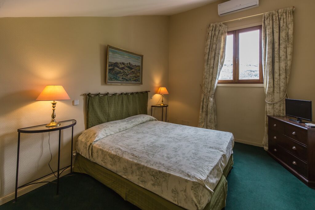 A bedroom with a bed, two bedside lamps, a dresser, a painting on the wall, and a window with curtains.