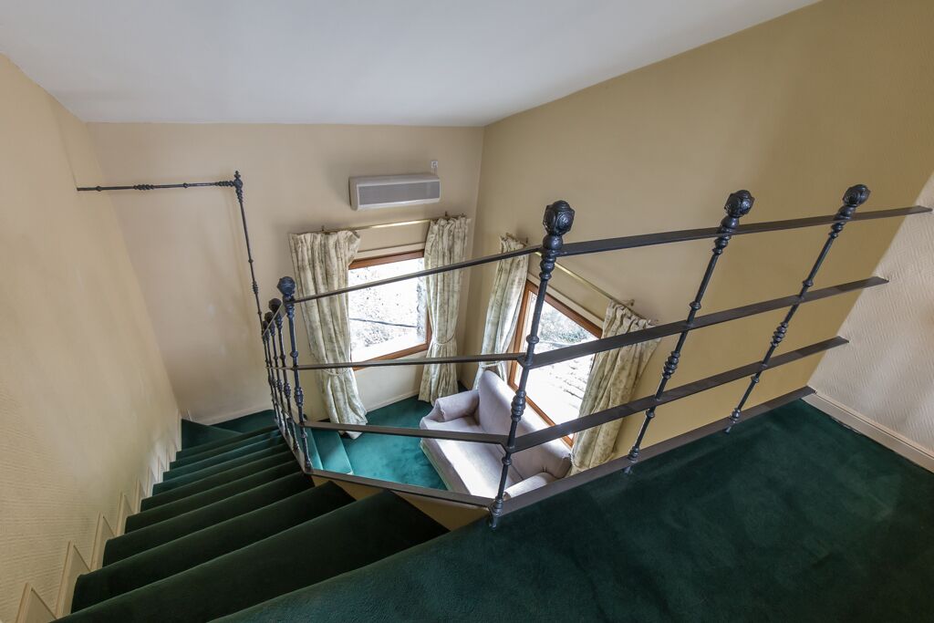 Una escalera con alfombra verde que conduce a una habitación con un sofá y cortinas.