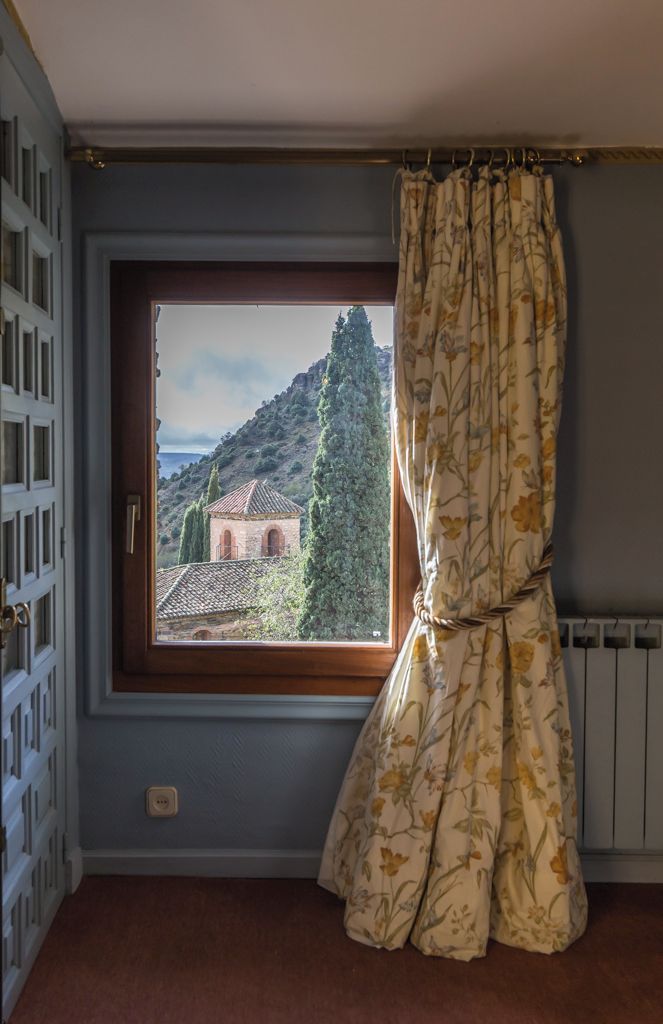 A room with a window, a curtain, and a view of a building and trees.