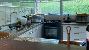 Une cuisine moderne avec des armoires blanches, une hotte de cuisinière en acier inoxydable, un four encastré et une fenêtre donnant sur la verdure à l’extérieur.