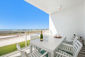 En balkon med et hvidt bord dækket til to, med udsigt over en strand.