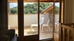 Ein Balkon mit Blick auf einen bewaldeten Hügel, ein weißer Plastikstuhl und ein kleiner Tisch.