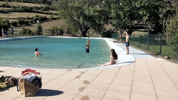 Ein Schwimmbecken mit Personen in der Nähe, einer gefliesten Liegefläche und Blick auf eine hügelige Landschaft.