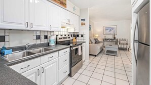 A modern kitchen with white cabinets, a stainless steel refrigerator, and a tiled floor. - LJ's Cottages 3 - BALCONY BEACH POOL SAND SUNSETS (Sarasota)