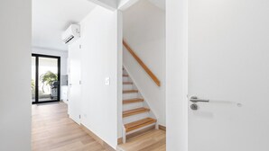Een modern interieur met een houten trap, witte muren en een zichtbare airconditioning.