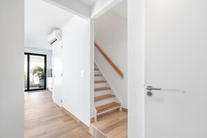 A modern interior with a wooden staircase, white walls, and a visible air conditioning unit. - Beautiful 3BR Townhouse near Palm Beach (Noord)