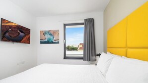 Een hotelkamer met een bed, een raam met gordijnen en twee kunstwerken aan de muur.