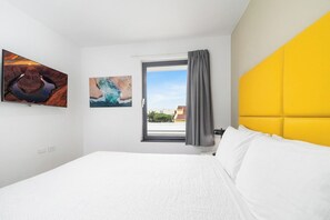 A hotel room with a bed, a window with curtains, and two wall-mounted artworks. - Beautiful 3BR Townhouse near Palm Beach (Noord)