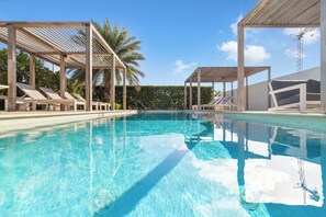 A clear swimming pool with sun loungers and shaded areas, surrounded by greenery. - Beautiful 3BR Townhouse near Palm Beach (Noord)