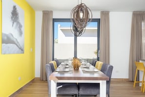 A dining area with a table set for four, a modern pendant light, and a large window with curtains.