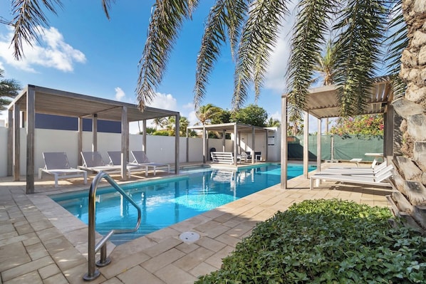 A swimming pool with lounge chairs and a covered seating area.