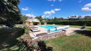 Une piscine entourée d’un mur de pierre et de verdure, avec des chaises longues et des parasols.