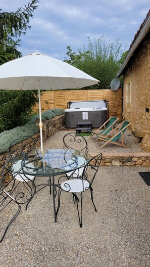 Une terrasse avec une table et des chaises en verre, un parasol blanc et un jacuzzi.