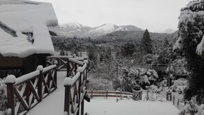 Eine mit Schnee bedeckte Holzterrasse mit Blick auf schneebedeckte Bäume und Berge im Hintergrund.