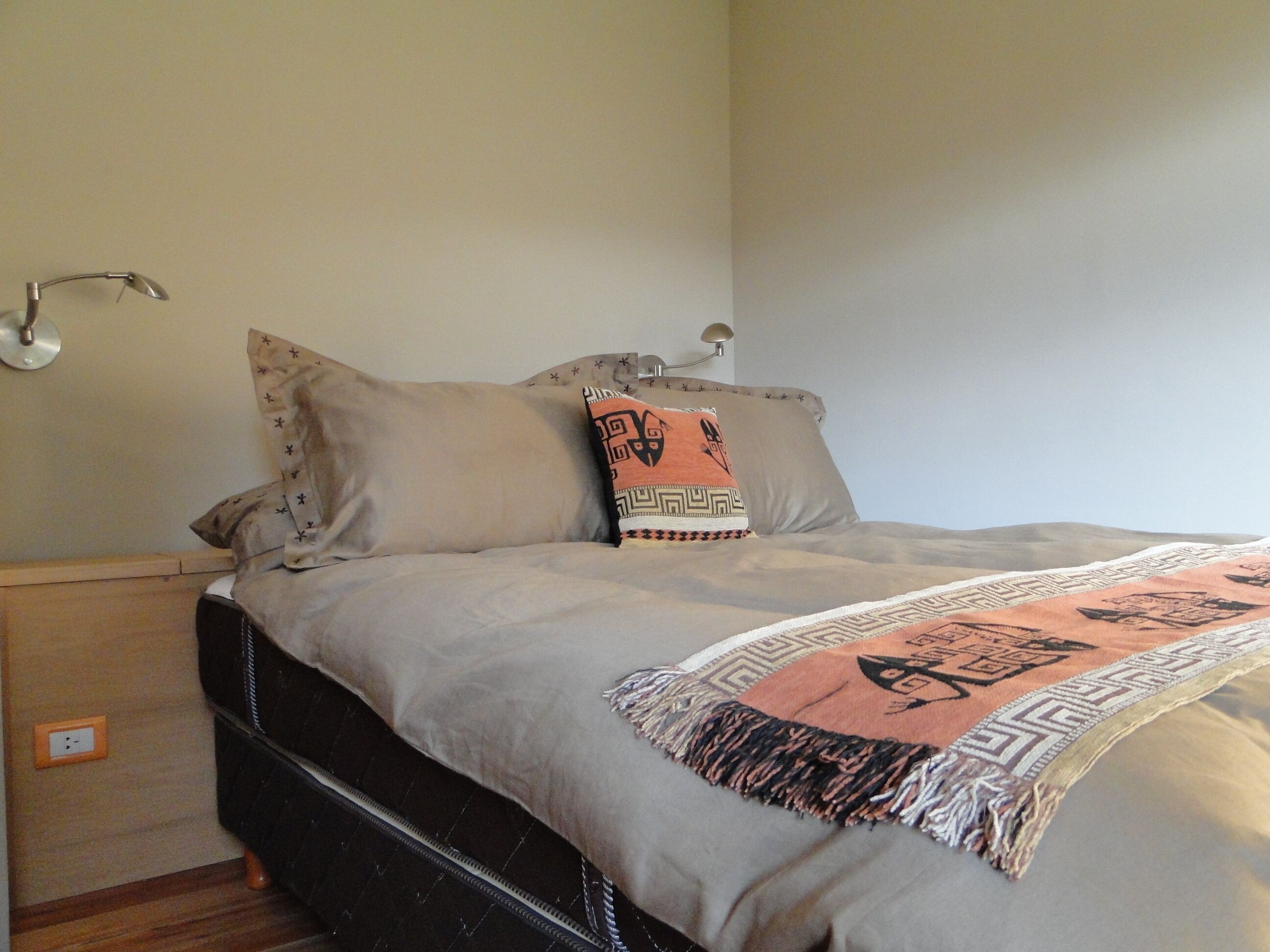 A bed with a patterned throw, two pillows with star designs, and a wall-mounted lamp.