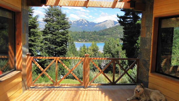 Eine Holzterrasse mit Metallgeländer, die auf eine Berglandschaft mit einem See blickt.