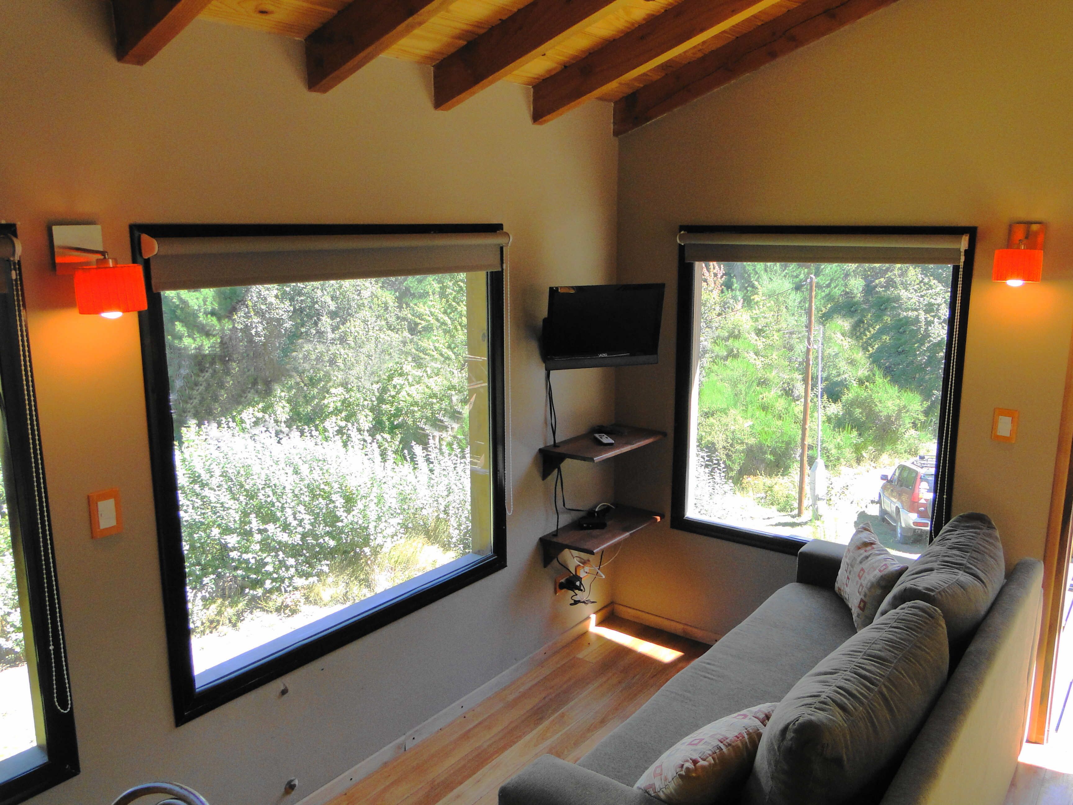A modern living room with large windows, a flat-screen TV, and a sofa.