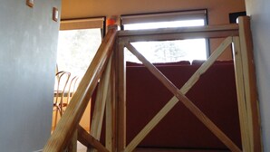 Ein Zimmer mit schrägverlegtem Holzboden, einem Fenster mit Aussicht und einer roten gepolsterten Bank.