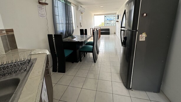 A kitchen with a dining area, a refrigerator, and a window with curtains. - My place in paradise (Puerto Baquerizo Moreno)