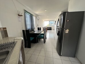 A kitchen with a dining area, a refrigerator, and a window with curtains. - My place in paradise (Puerto Baquerizo Moreno)