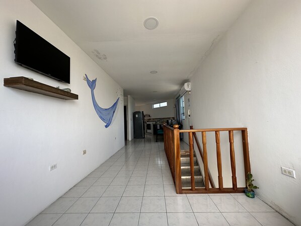 A hallway with a wooden staircase, a mounted TV, and a wall mural. - My place in paradise (Puerto Baquerizo Moreno)