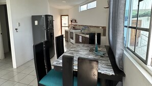A dining area with a tiled floor, a table with chairs, a refrigerator, and a window with curtains. - My place in paradise (Puerto Baquerizo Moreno)