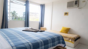 Een slaapkamer met een bed, een raam, gordijnen, een airconditioner en een klein tafeltje.