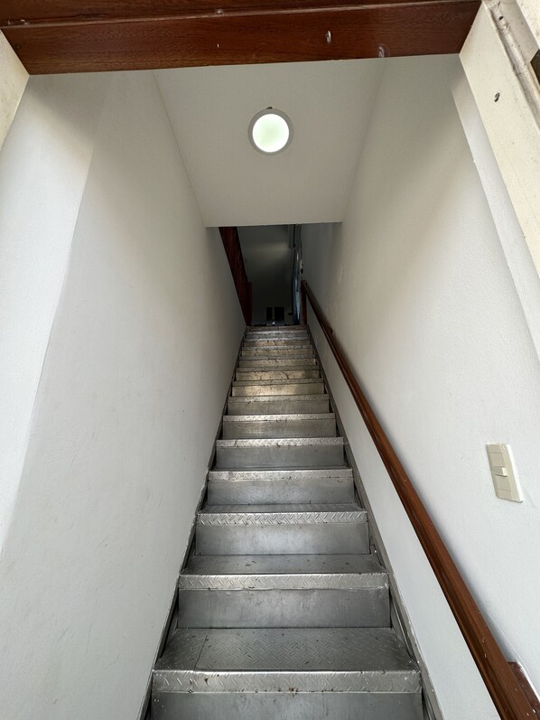 A narrow staircase with metal steps and wooden handrails, leading to a landing with a ceiling light. - My place in paradise (Puerto Baquerizo Moreno)