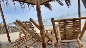 A beach with bamboo lounge chairs and a thatched roof structure. - Las Fragatas Casa Hotel  (Canoas de Punta Sal)